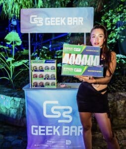mujer al lado de un stand de geek bar sosteniendo un muestrario de productos