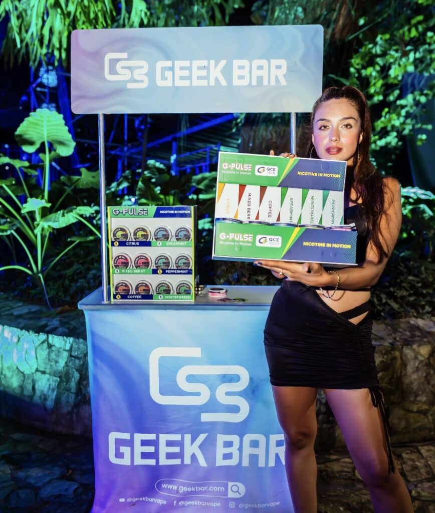 mujer al lado de un stand de geek bar sosteniendo un muestrario de productos