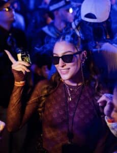 mujer joven en una fiesta con anteojos de sol y un vape en la mano